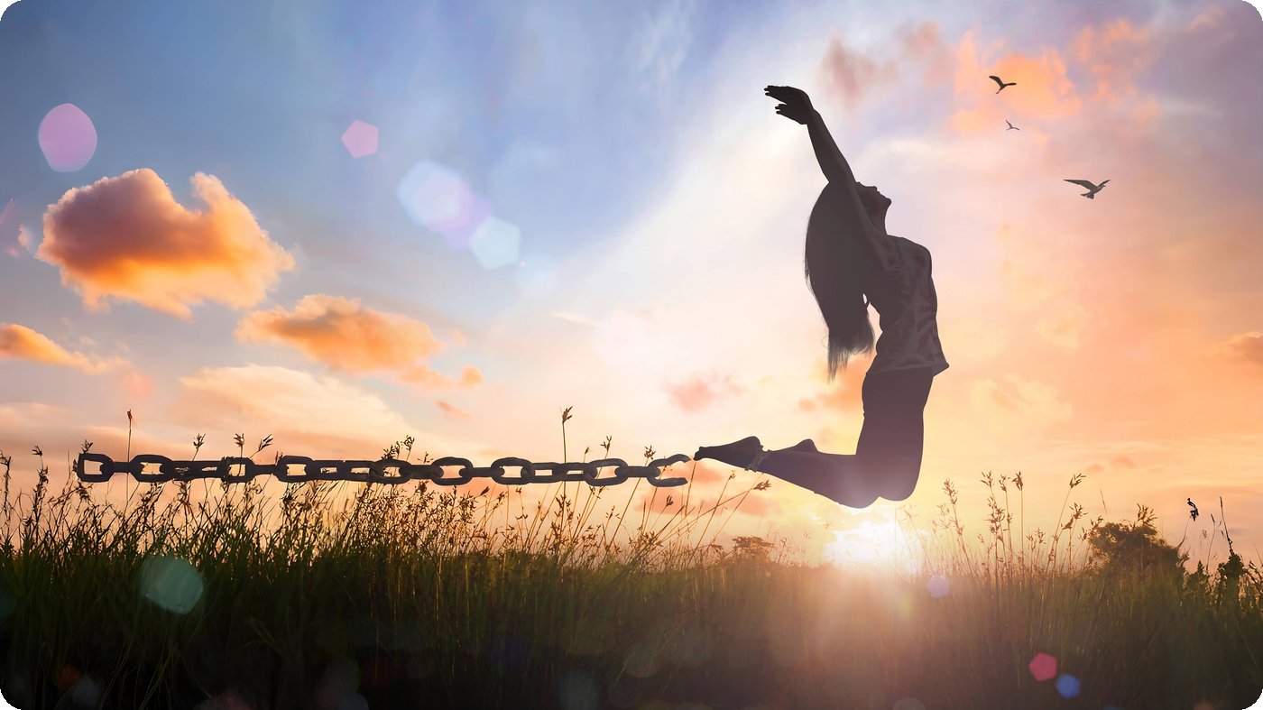 A woman leaping freely in a field at sunset, a broken chain trailing from her ankle